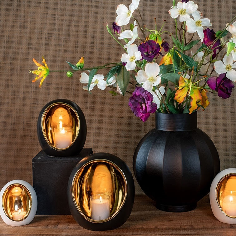 Zwarte theelichthouder met gouden kaarsglas, brandend kaarsje op houten plank