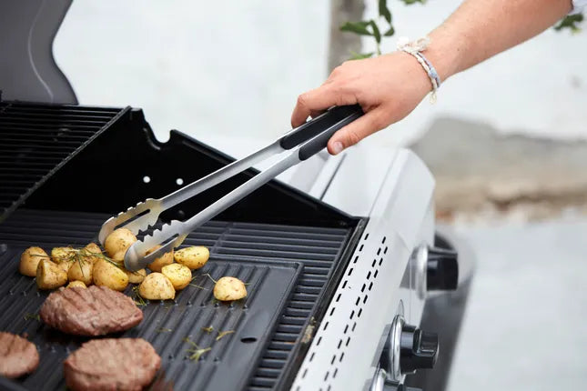 Barbecook universele barbecue-tang in gebruik boven de grill, rvs en zwarte handgrepen