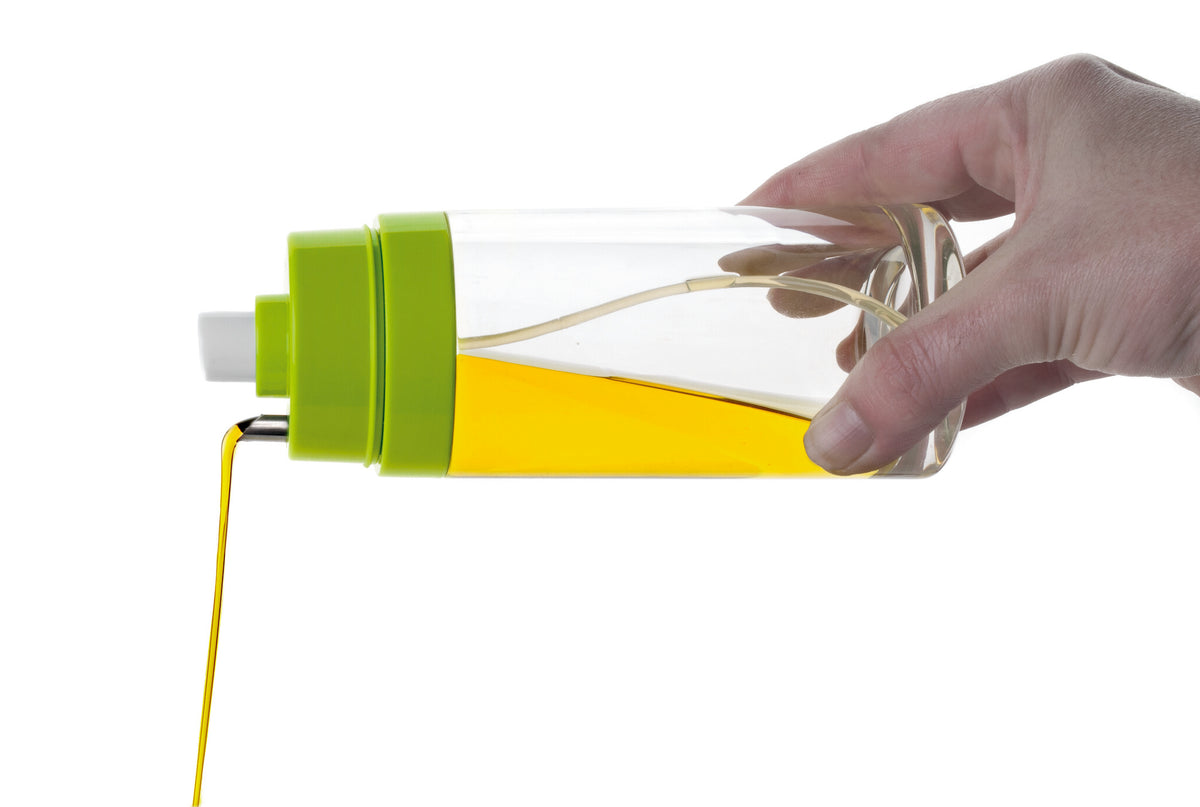 Olie- en azijnsprayer met groene knop, hand draait spuitdeel boven gele vloeistof.