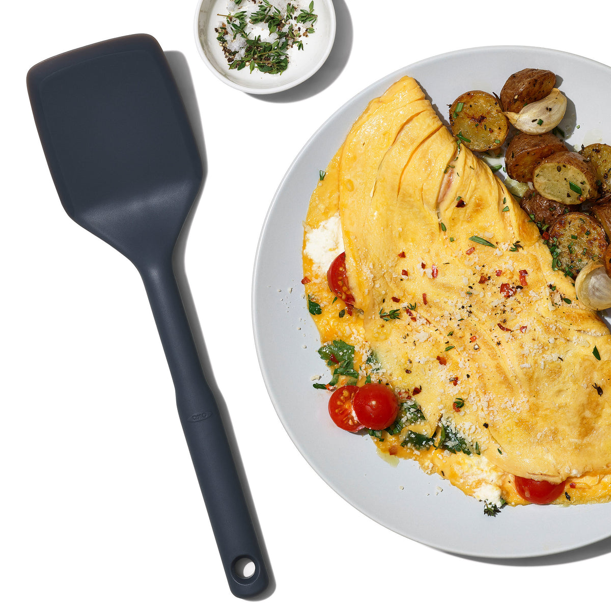 OXO siliconen spatel naast bord met gerecht, donkergrijs