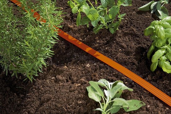 Oranje druppelslang in een beplantingsperk langs de grond