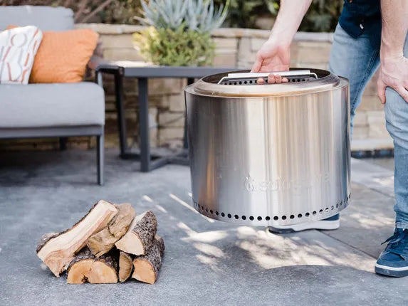 Solo Stove Bonfire vuurkorf met metalen handvat en stapel brandhout