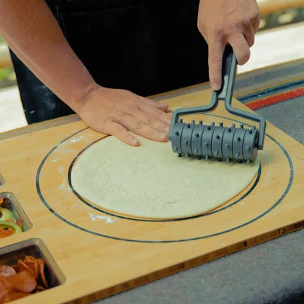Deegprikker met zwarte rolwielen, gebruikt op deeg op houten plank.