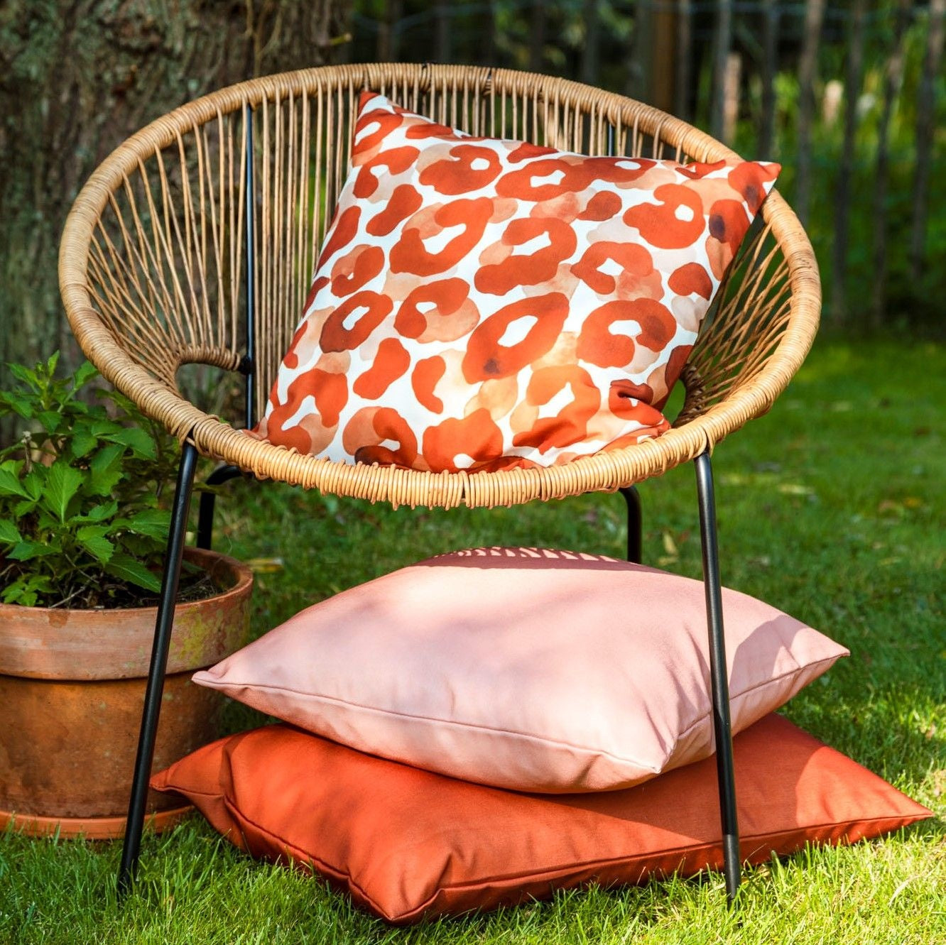 Sierkussen 45x45 cm in gemuteerde kleikleur op tuinstoel met rieten zitting.