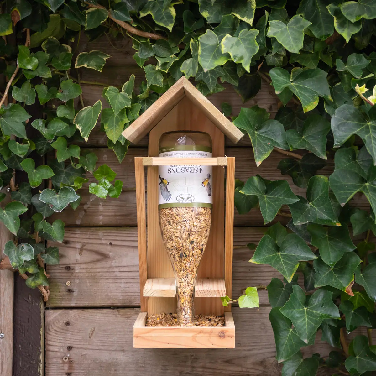 Voorzijde van houten vogelvoederhuis met gevulde wijnfles strooivoer