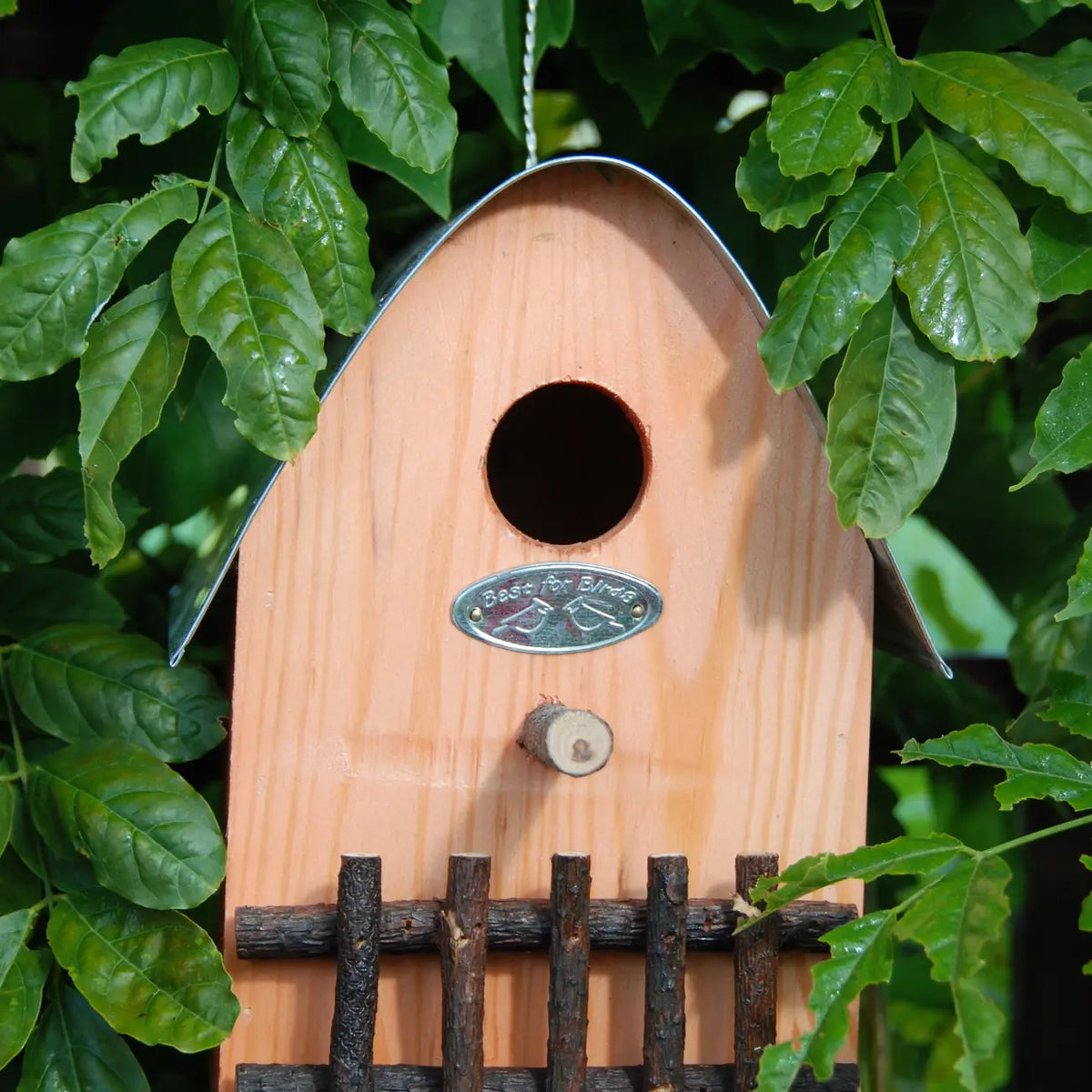Landelijke houten nestkast met ronde ingang, metalen plaat en houten spijlen aan de voorkant.