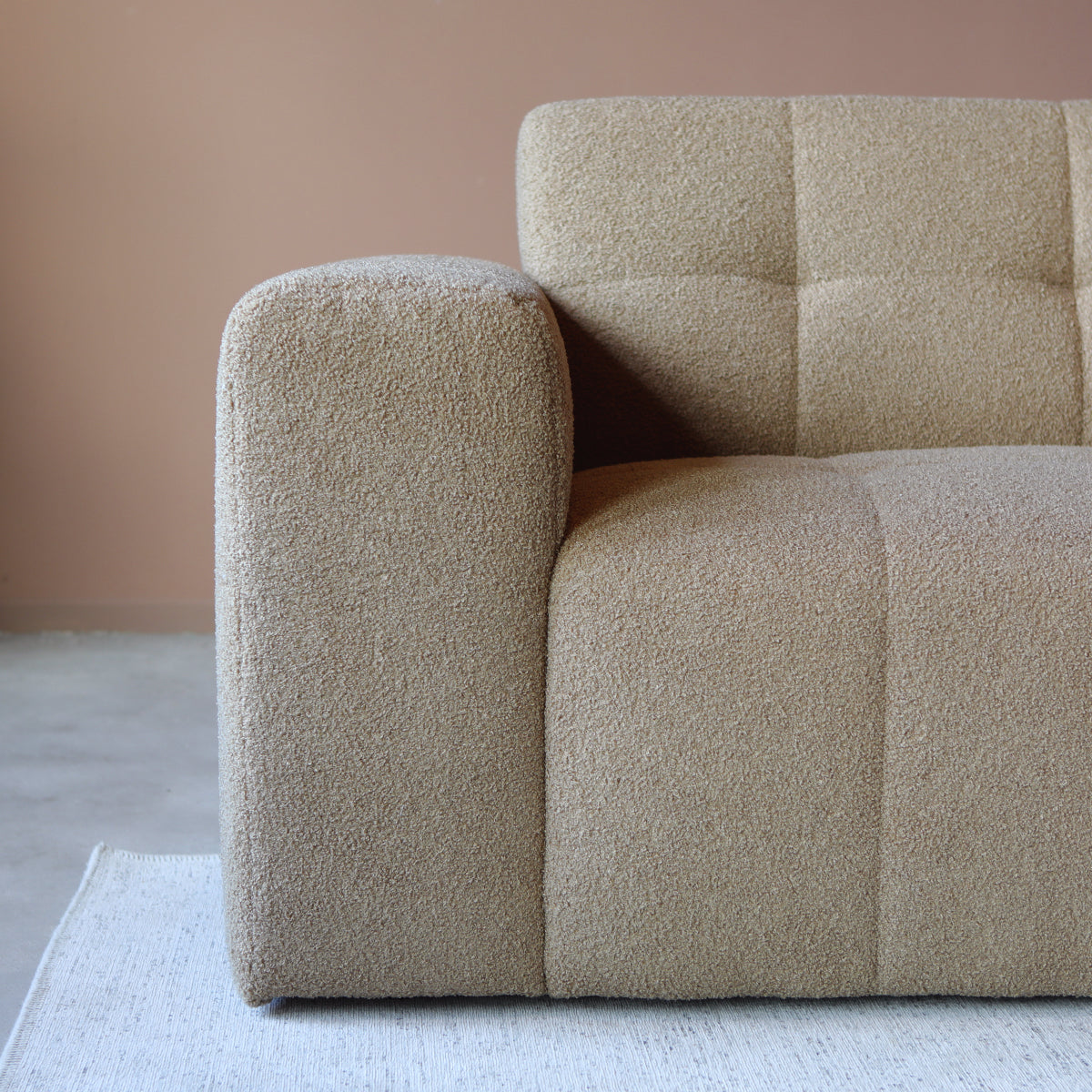 Beige chaise bank met brede armleuning en bouclé-achtige stofstructuur.