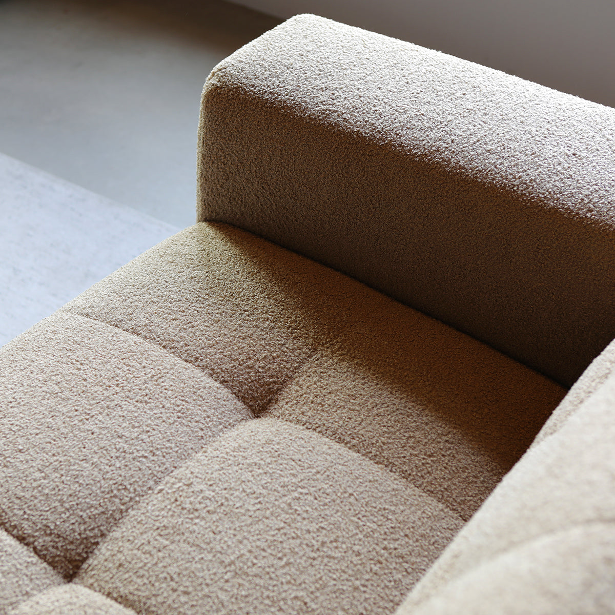 Beige zitbank met gestoffeerde blokkussens en brede rugleuning.