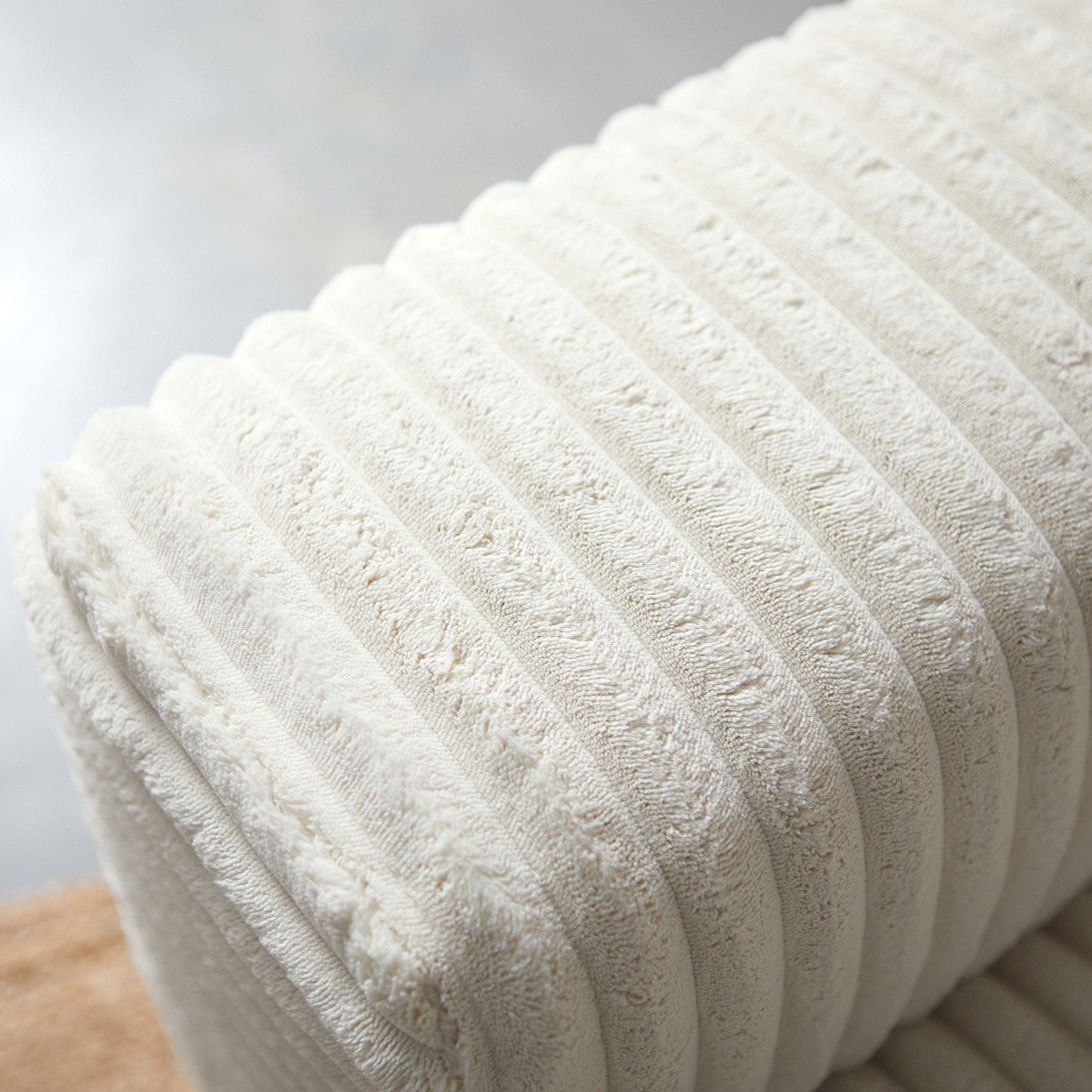 Detail van crème bankbekleding met geribbelde stofstructuur en afgeronde hoek.