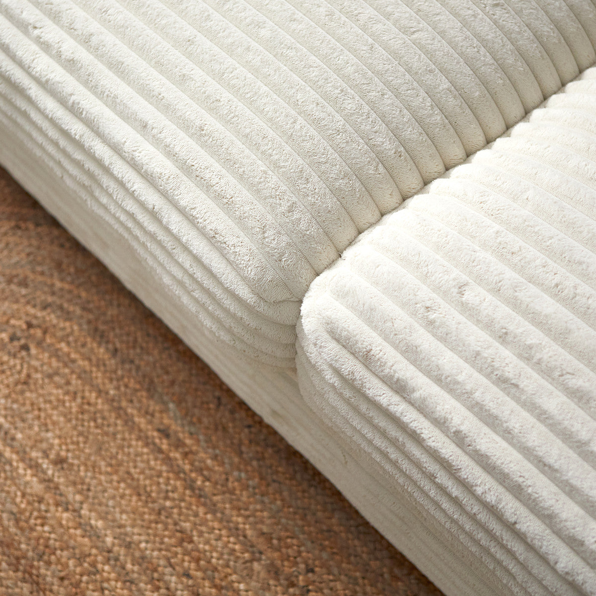 Detail van crème chaise longue met geribde zitting en rugkussens, naast bruin kleed.