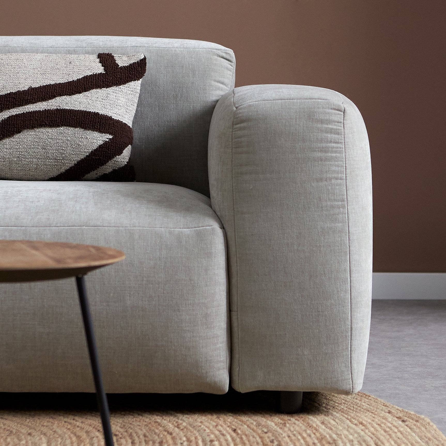 Lichtgrijze chaise longue armleuning met kussennaad en bijzettafeltje naast de bank.