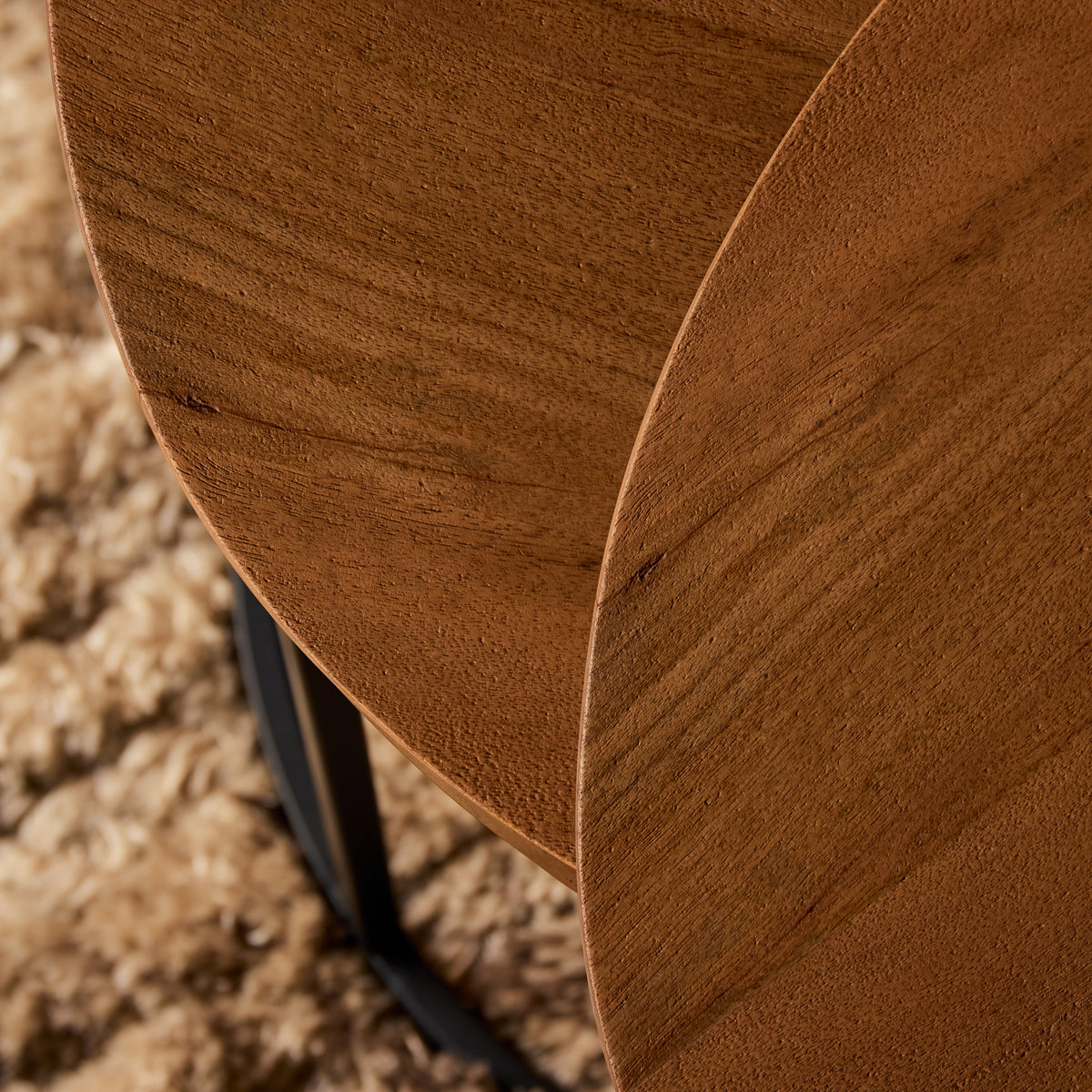 Hoek van rond naturel houten tafelblad met zwart metalen poot en strak frame