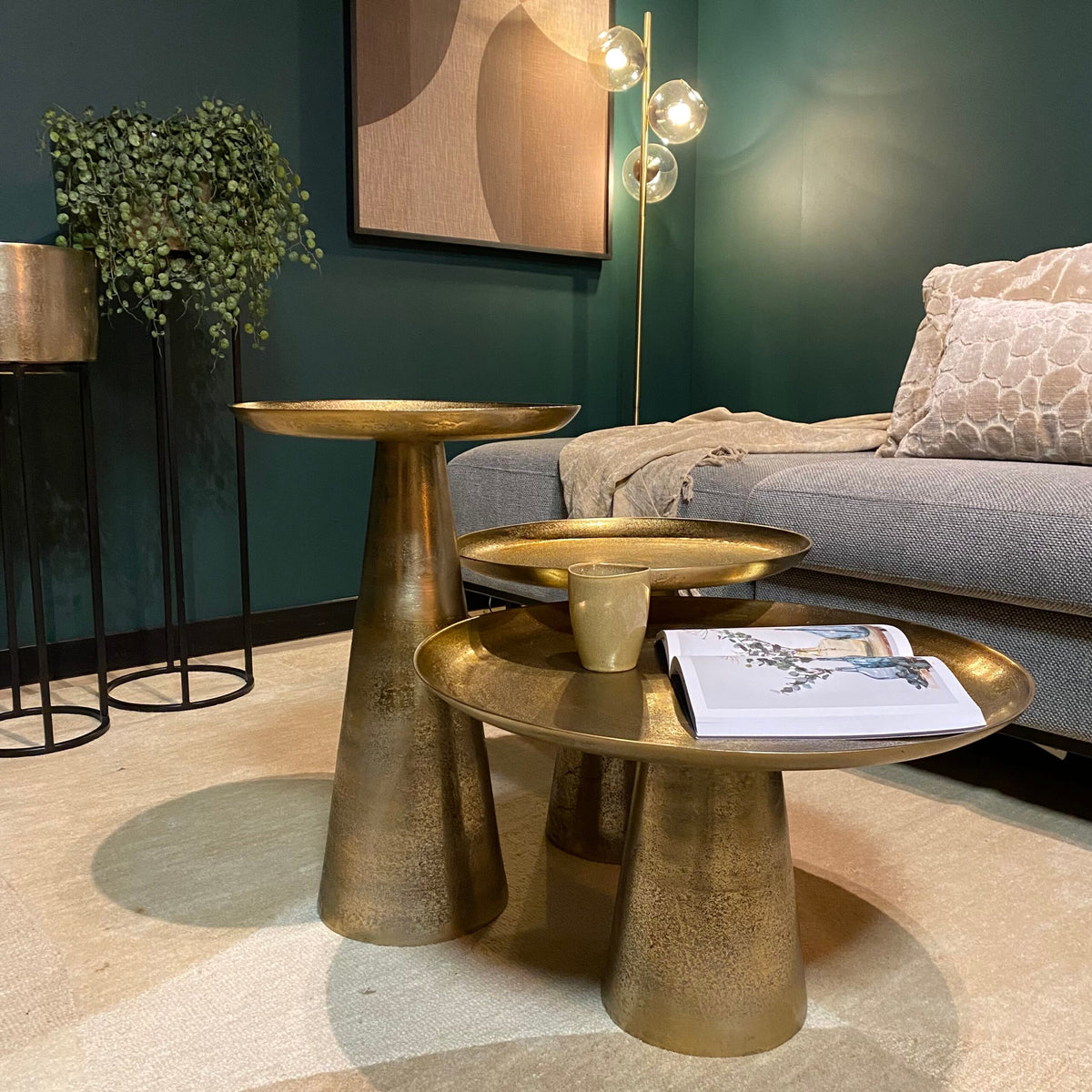 Gouden ronde salontafels met drie bladen, mok en tijdschrift op het voorste blad