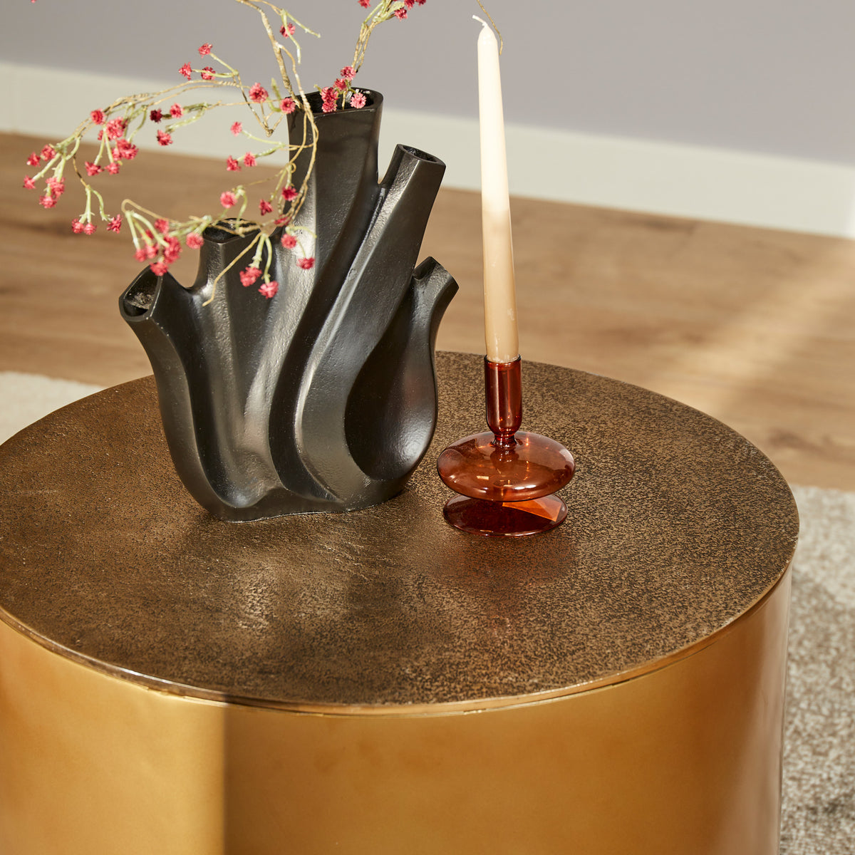 Gouden ronde salontafel Fiore met zwart metalen organisch stuk en staande kaars.