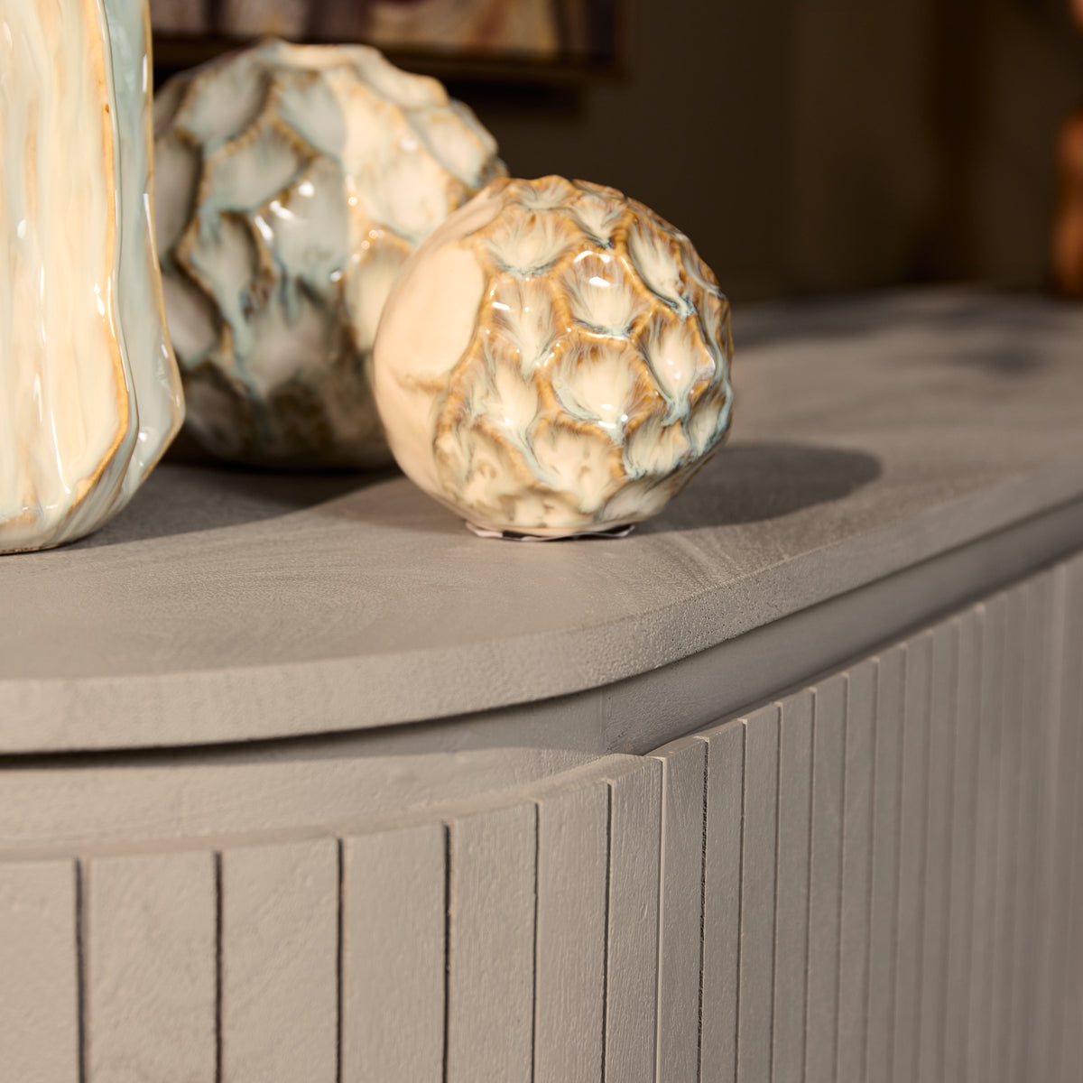Dressoir detail: geribbelde zijpanelen met afgeronde bovenrand, grijs-taupe tint.