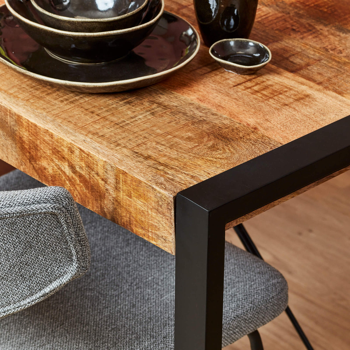 Eettafel met houten blad en zwarte metalen poten, hoekdetail met randafwerking.