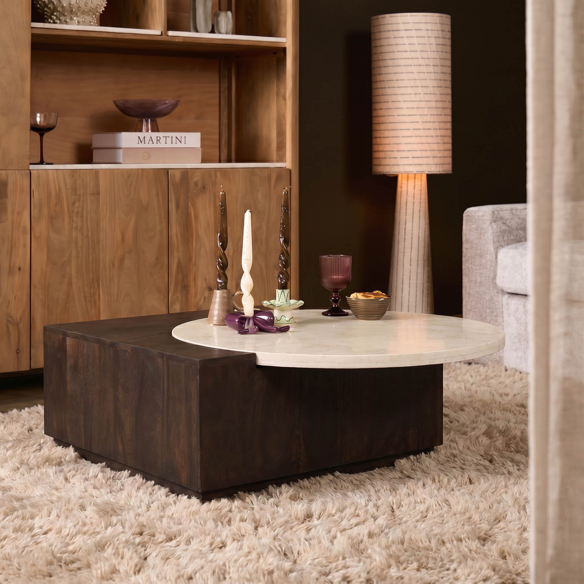 Salontafel met rond licht steenkleurig blad en houten basis, in woonsetting met kleed.