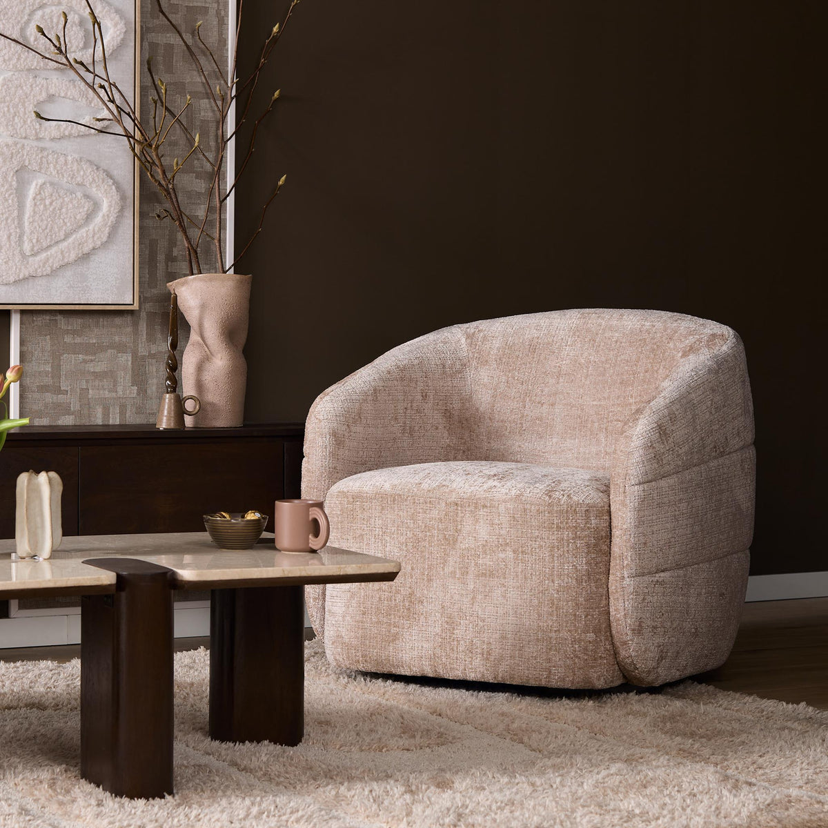 Beige gestoffeerde fauteuil met ronde rug en armleuningen, dikke zitting en organische vorm.