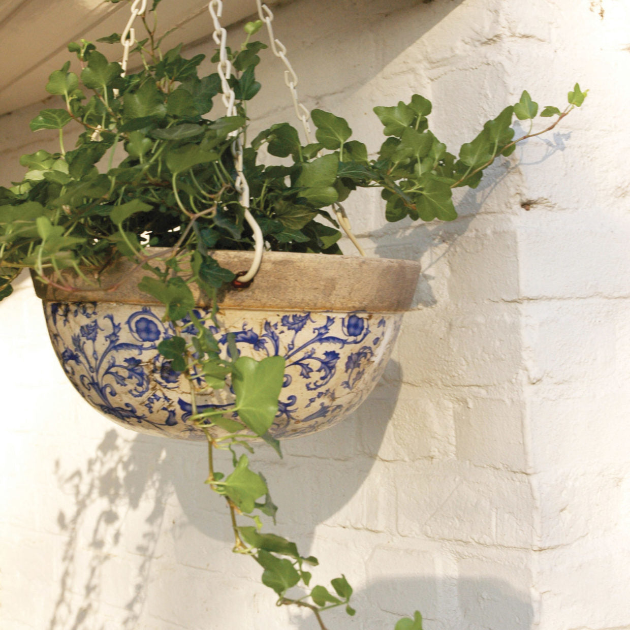 Hangende keramische mand blauw-wit met ophangkettingen, gevuld met groene planten