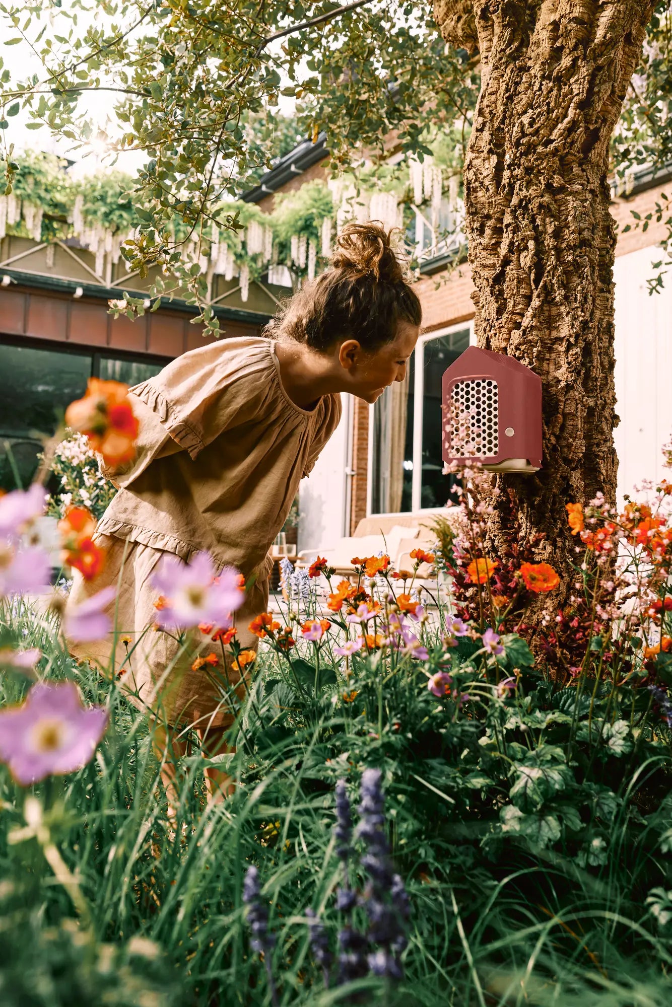 Rood insectenhotel aan een boomstronk in een tuin met bloemen