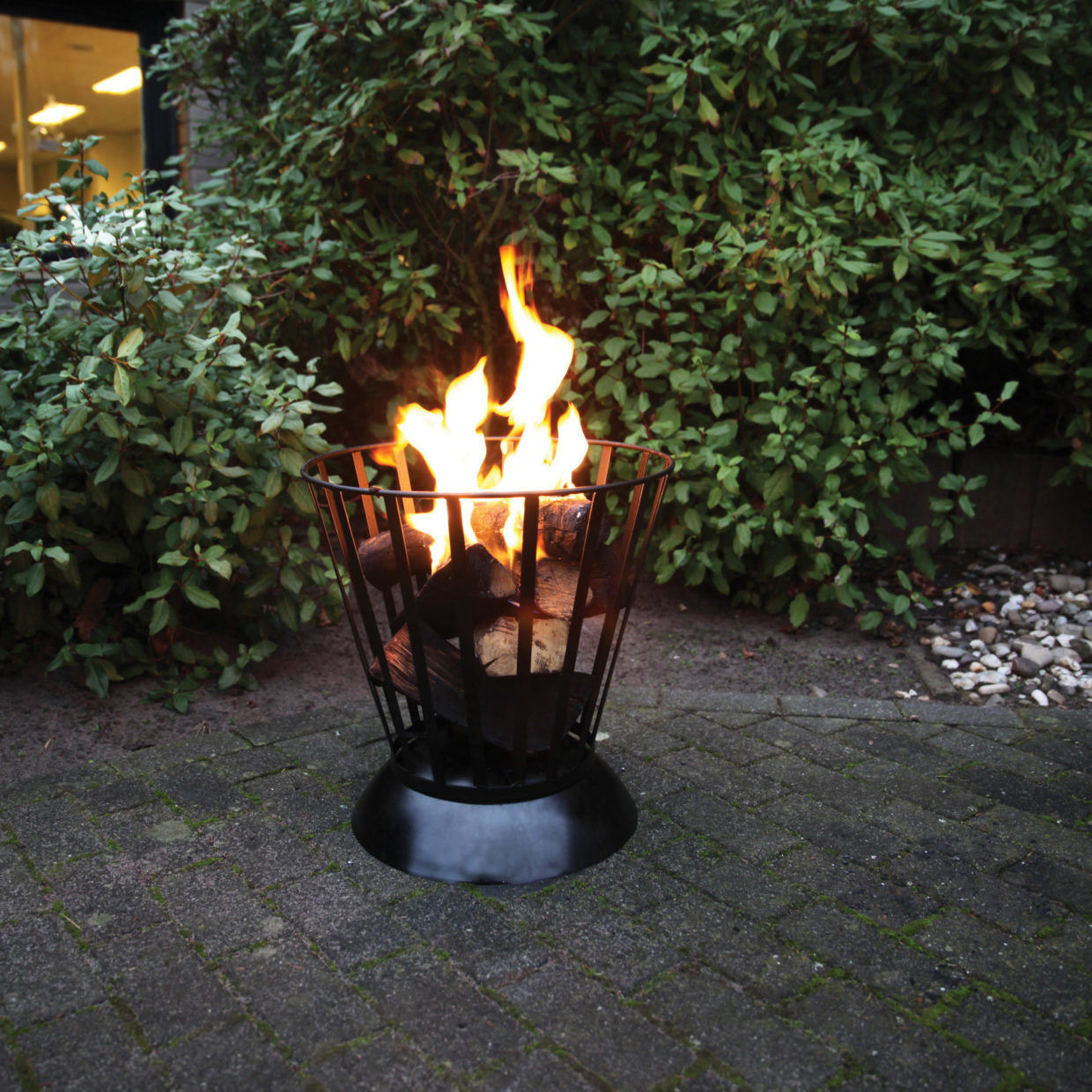 Vuurschaal met zwarte draadkorf en brandende vlammen, met houtblokken zichtbaar