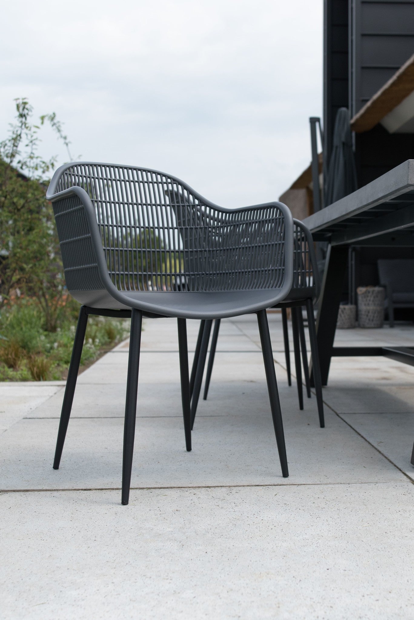Grijze tuinstoel met armleuningen en verticale lattenrug, slanke pootjes