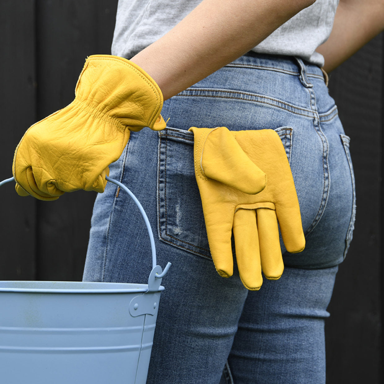 Gele leren tuinhandschoenen aan handen, met duim en vingers zichtbaar