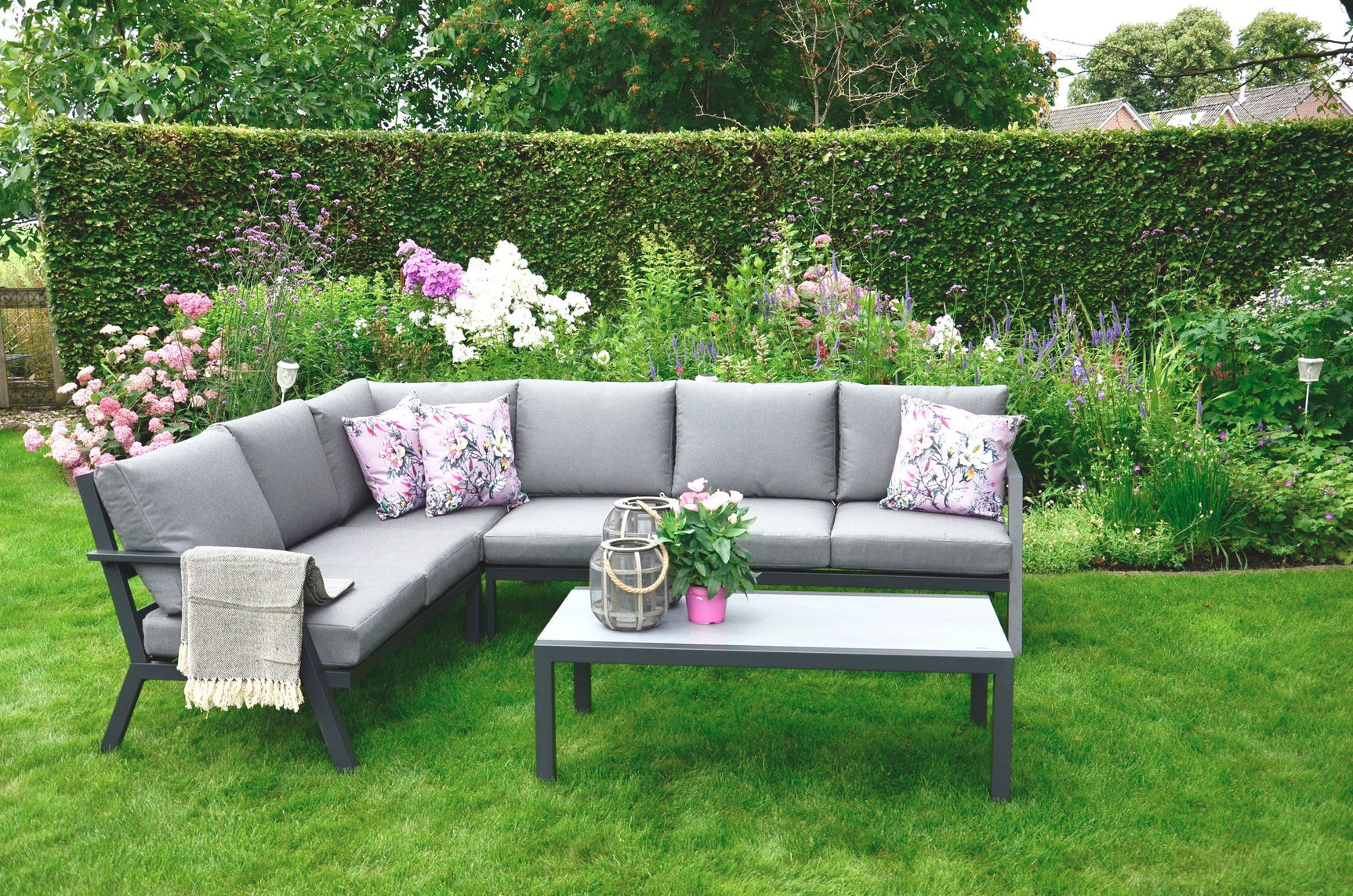 Loungehoekset met lichtgrijze bank en salontafel, sierkussens met bloemenprint.