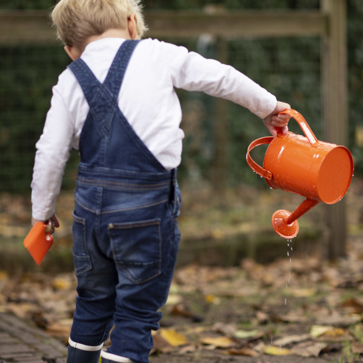 Oranje kindergieter met waterstraal, vastgehouden door een kind.