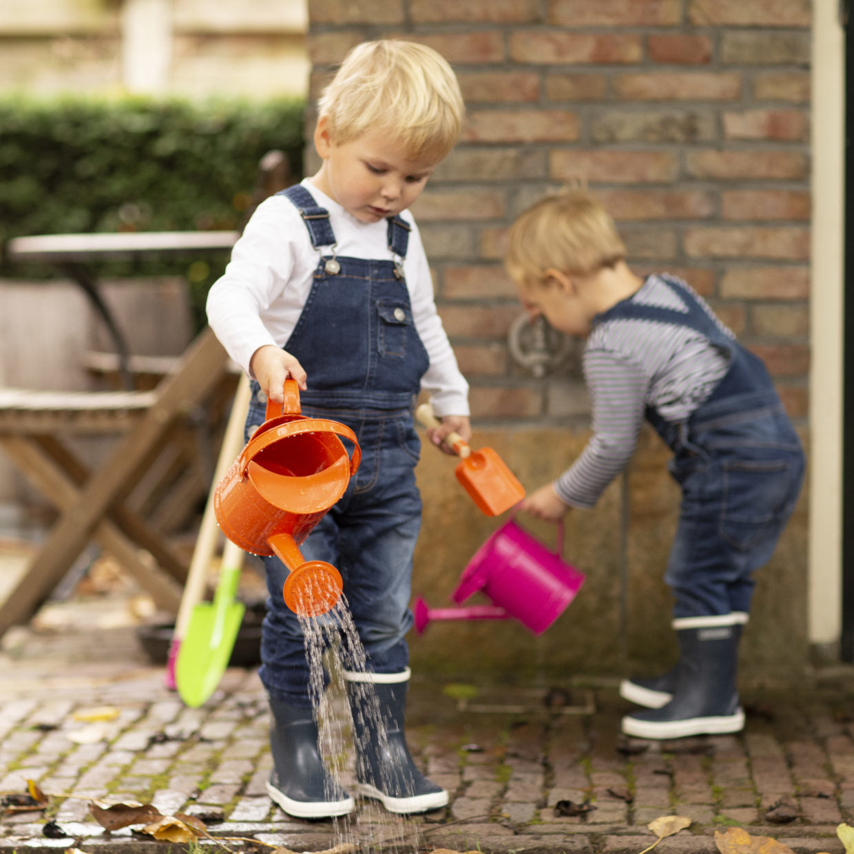 Kinderen met oranje en roze kindergieters, water stroomt uit de tuit.
