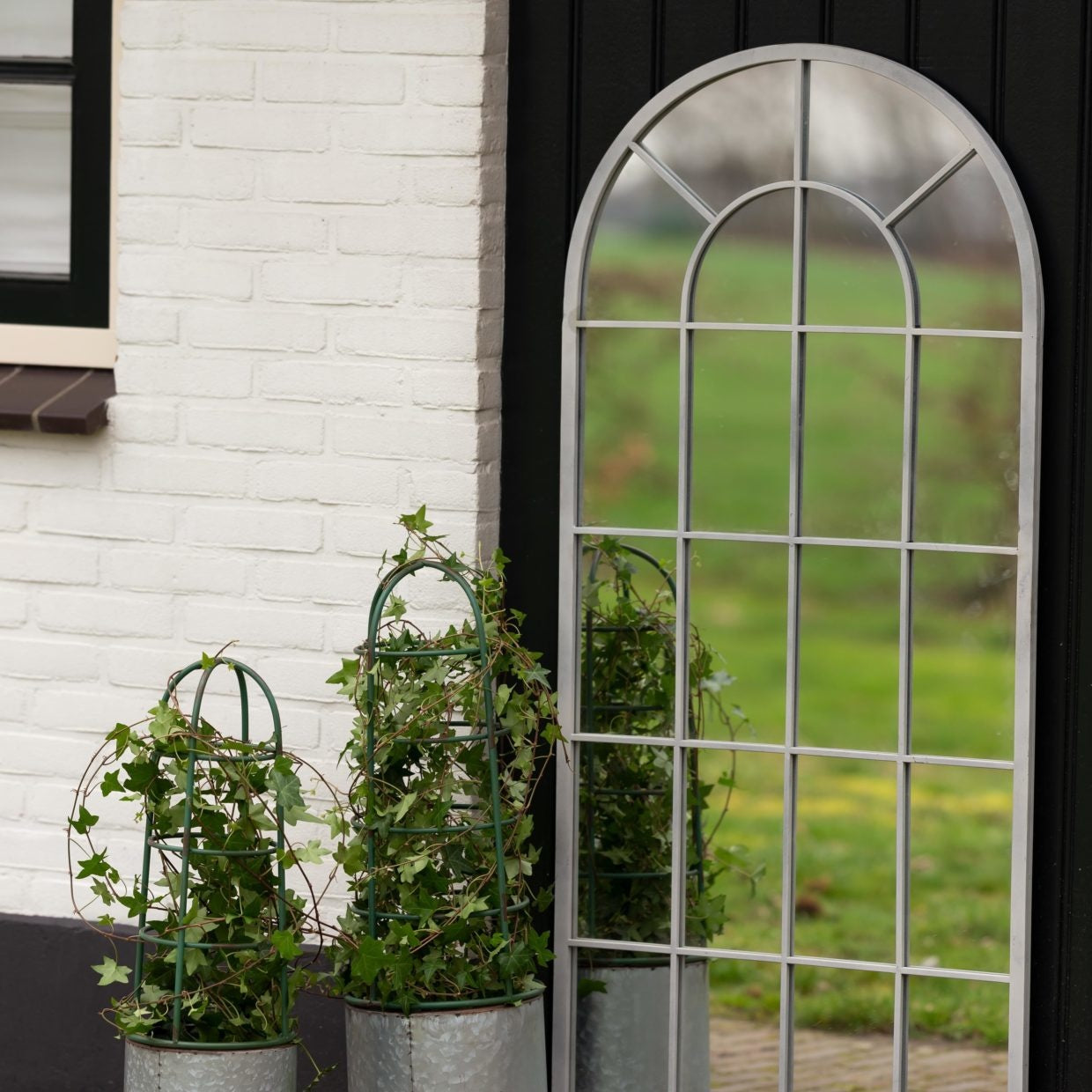 Bloembak met plantensteun en groene plant in een grijze pot met boogrek