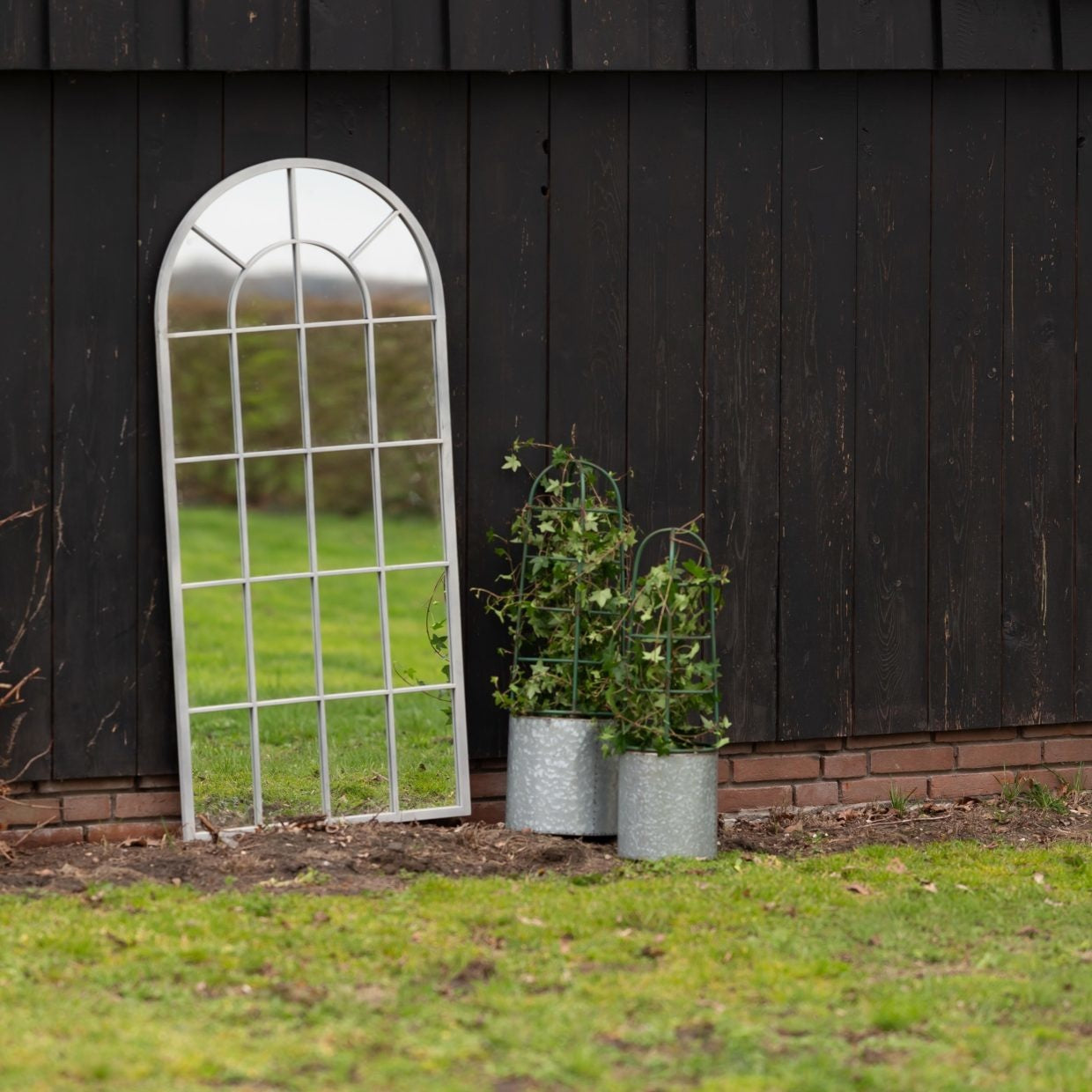 Twee grijze bloempotten met plantensteun en groene stengels in pot