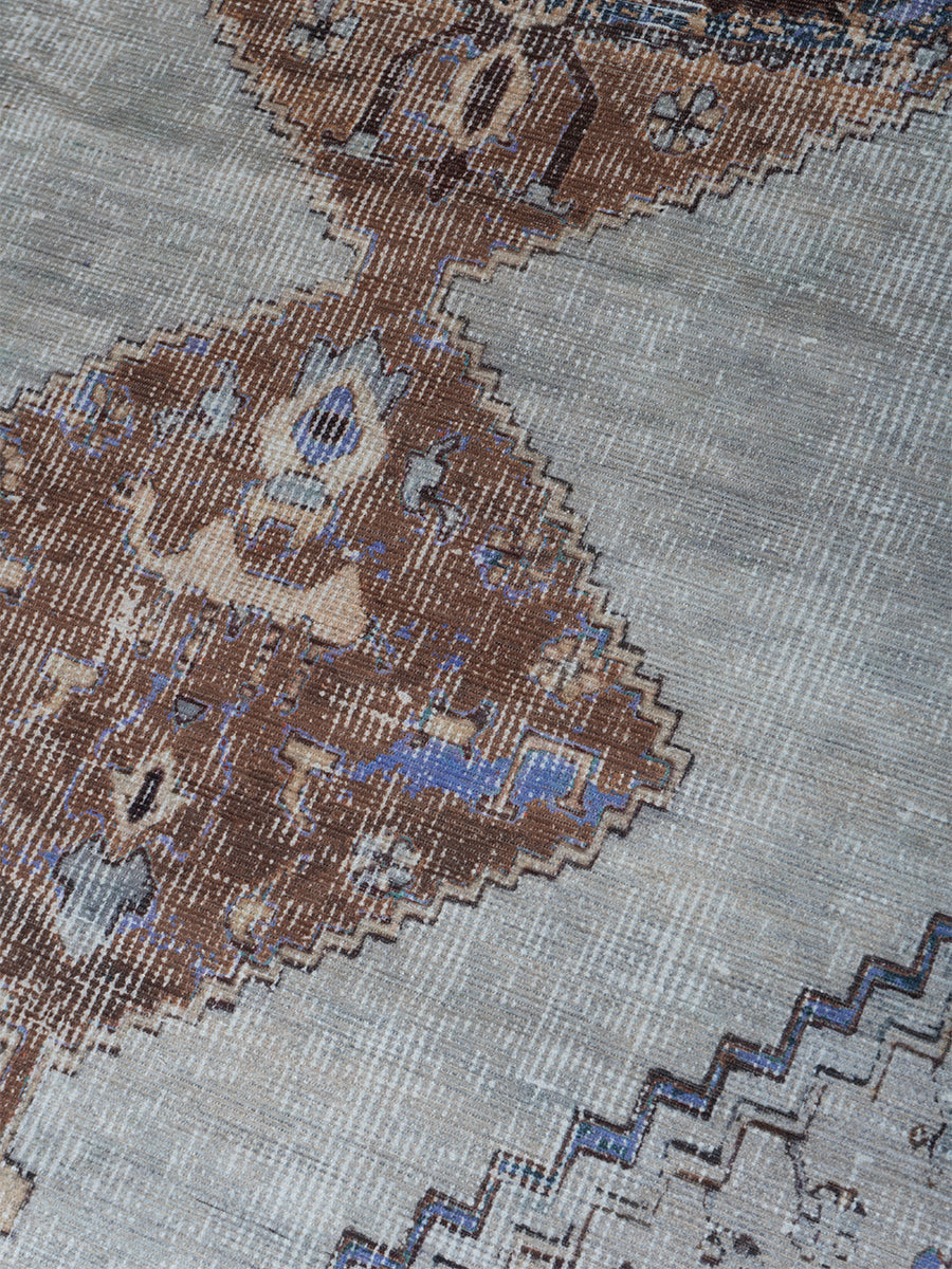 Vloerkleed close-up met lichtgrijs, bruin en blauw geometrisch motief en weefstructuur