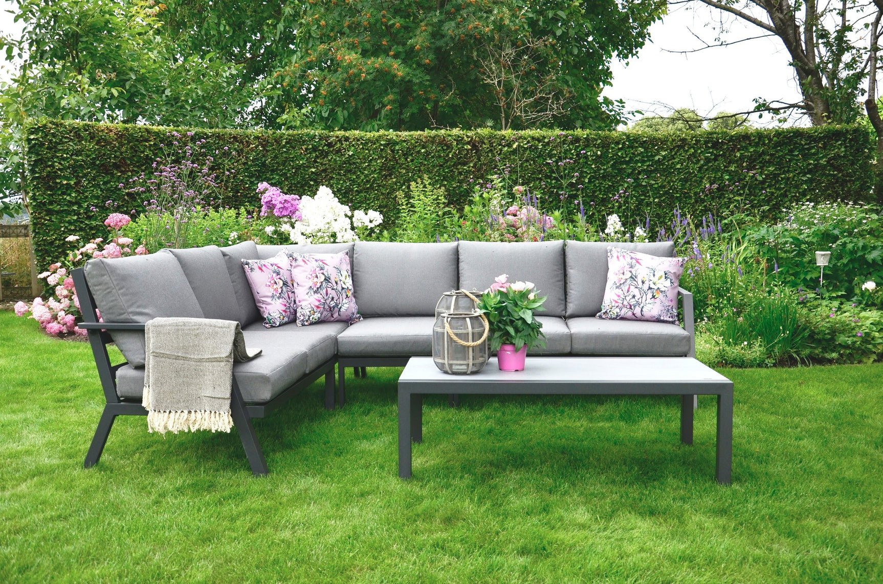 Loungehoekset met lichtgrijze bank, salontafel en bloemenprint sierkussens, plaid op arm.