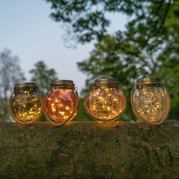 Vier glazen zonne-LED lantaarns met amberkleurig licht, op steen