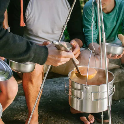 RVS vuurkorf op driepoot met pan en kettingen, koken met lepel en pan