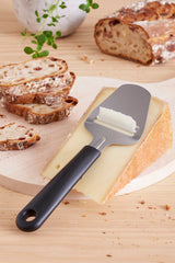 Kaasschaaf met zwart handvat en wit schraperblad naast kaas op plank