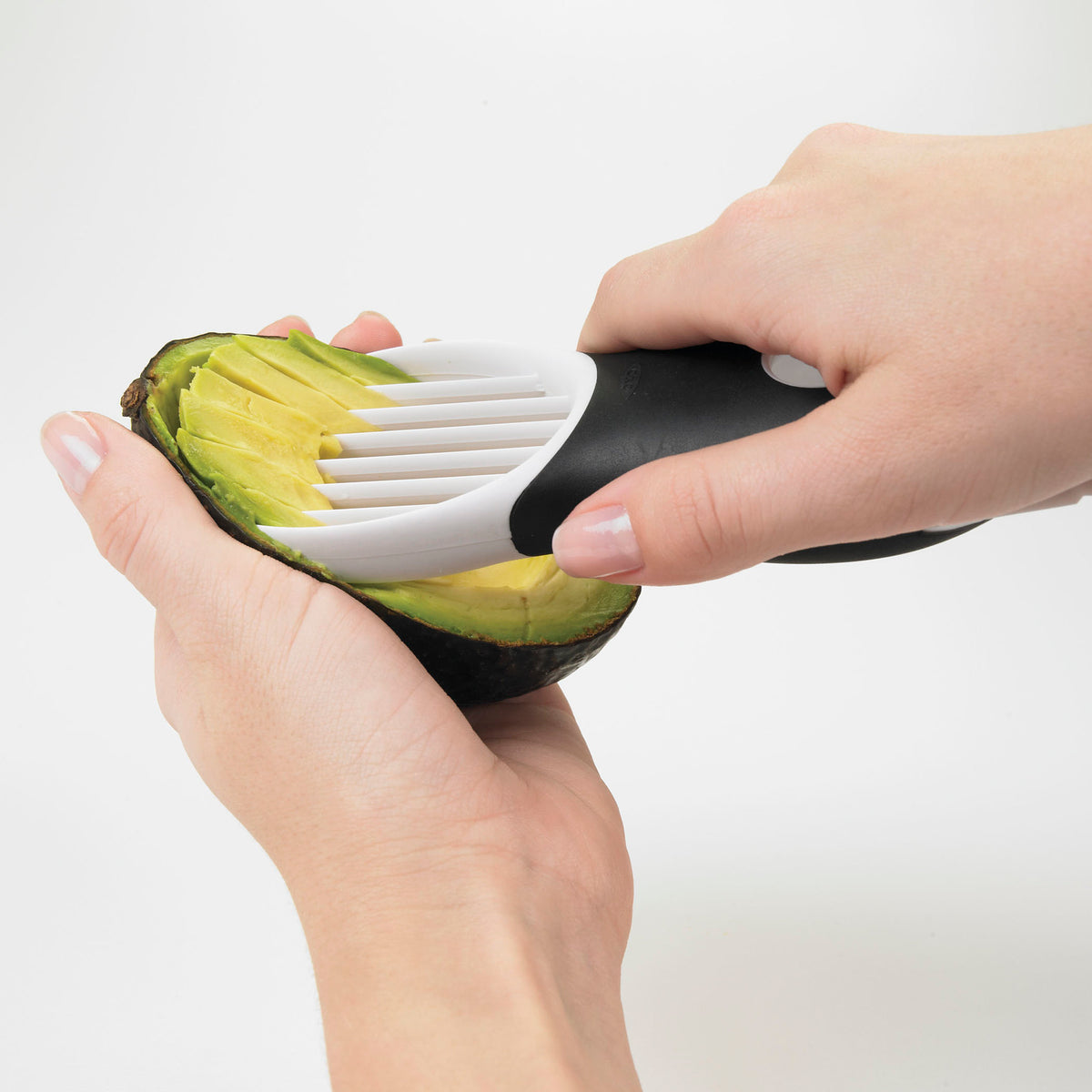 Avocadosnijder 3-in-1 snijdt avocado met witte tanden op zwarte beugel.