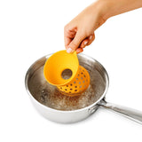 Hand plaatst een gele OXO eierpocheerder in een pan