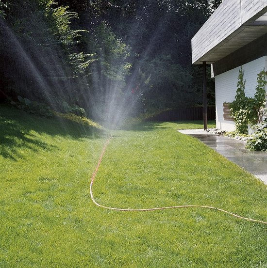 Oranje druppelslang die water sproeit over het gazon