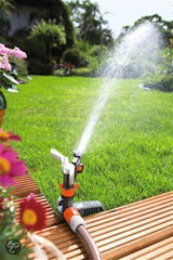 Tuin-cirkel sproeier met instelkop en waterstraal op gras en houten plank
