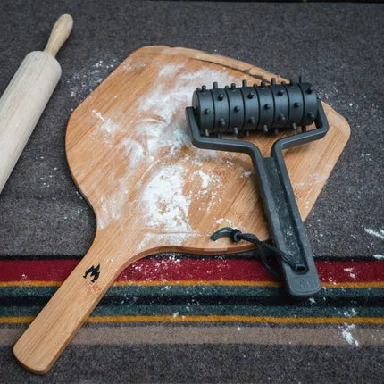Deegprikker met zwarte rollers op houten snijplank.