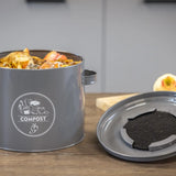 Keukencomposter antraciet met etensresten en losse bodemplaat met donkere compost.