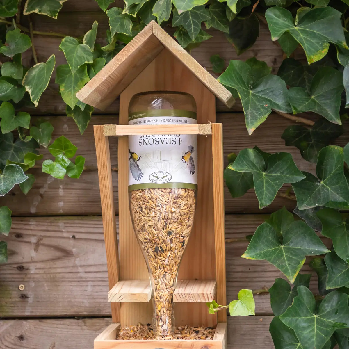 Houten vogelvoederhuis met gevulde wijnfles strooivoer