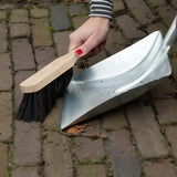 Metalen stofblik en houten veger met zwarte borstelharen, klaar om te vegen.