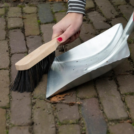Metalen stofblik en houten veger met zwarte borstelharen, klaar om te vegen.