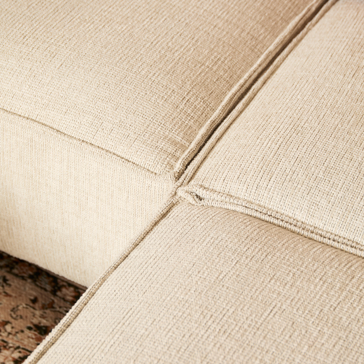 Beige divanbekleding met zichtbare stiknaden en geweven structuur, hoekdetail
