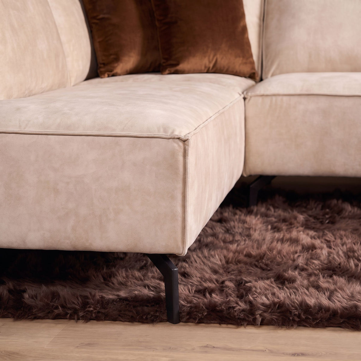 Beige fluwelen zitgedeelte met hoekdetail, bruine sierkussens en zwarte poot