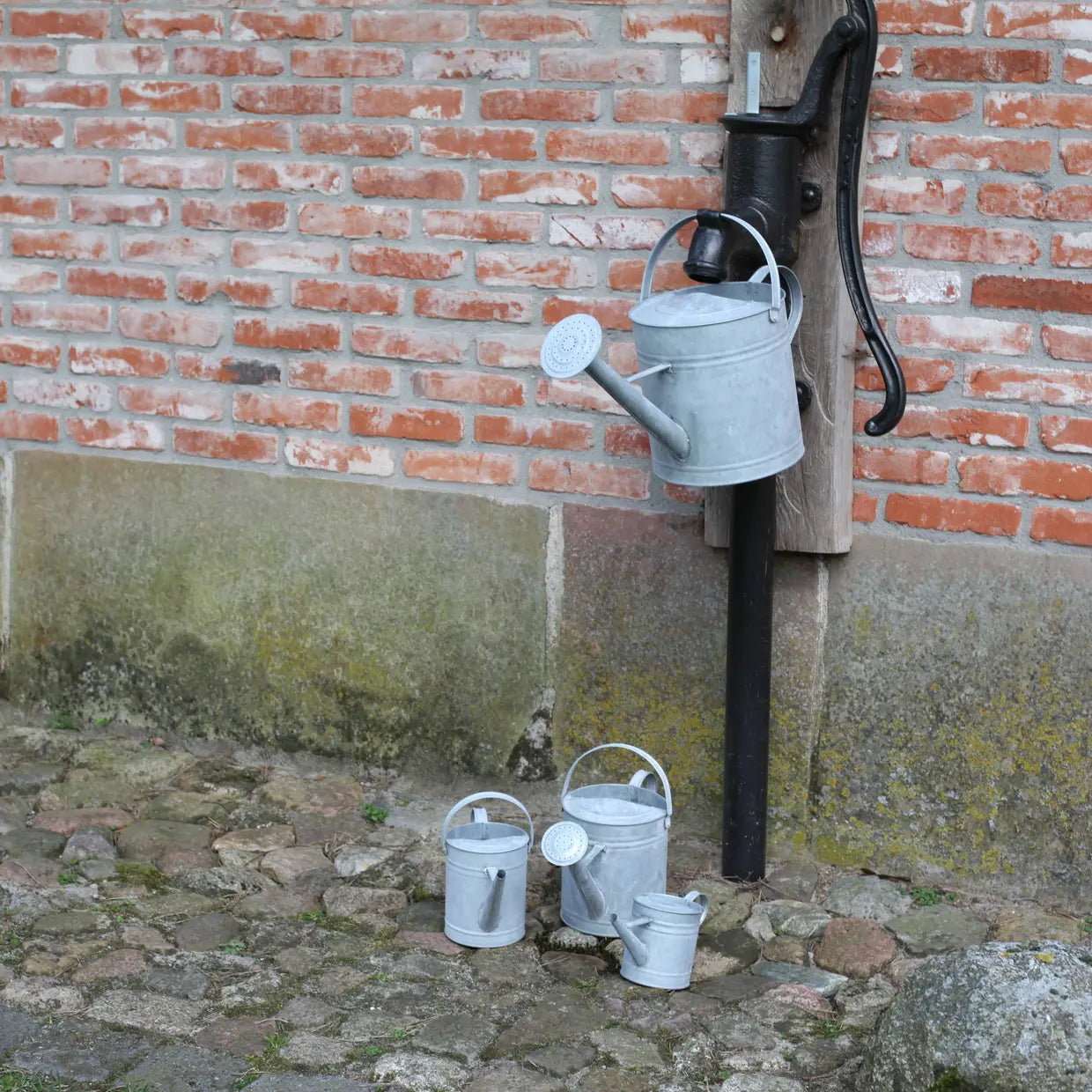 Zinken gieter met lange steel en sproeikop aan paal, vergrijsde afwerking
