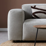 Lichtgrijze chaise longue bank met afgeronde armleuning en zwart-wit sierkussen.